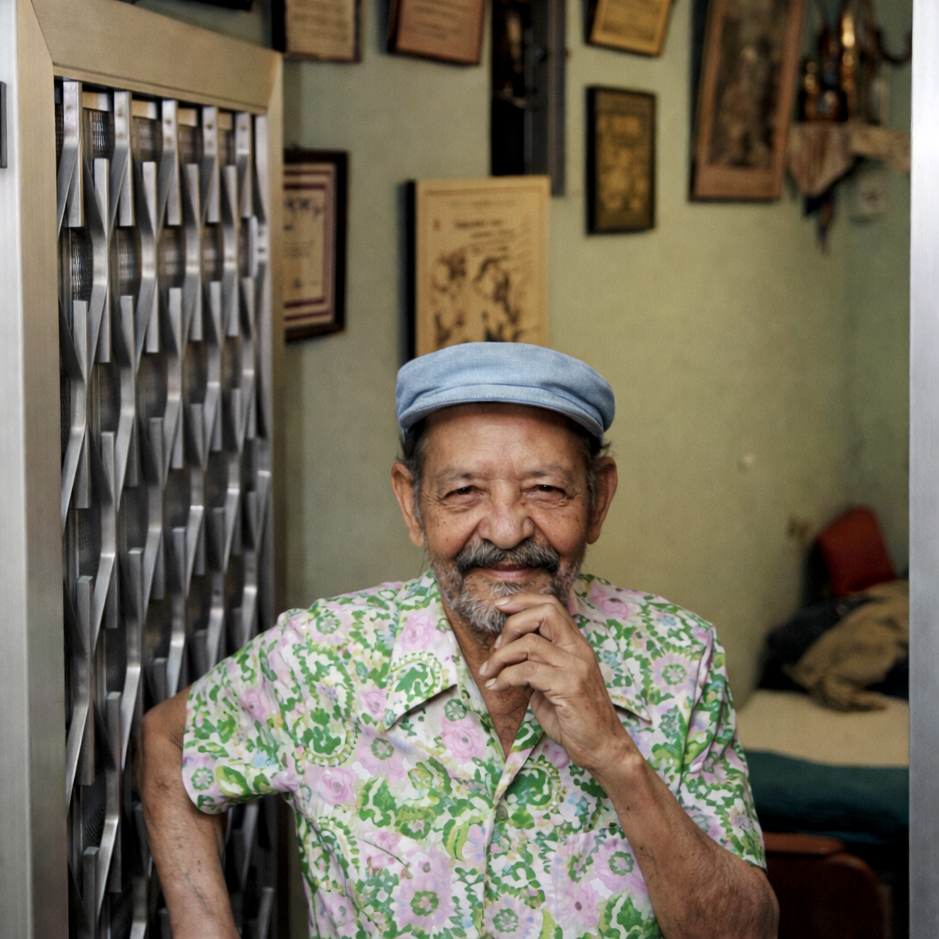 Carlos Cachaça de boina e camisa estampada sentado na soleira da porta de sua casa no morro de Mangueira