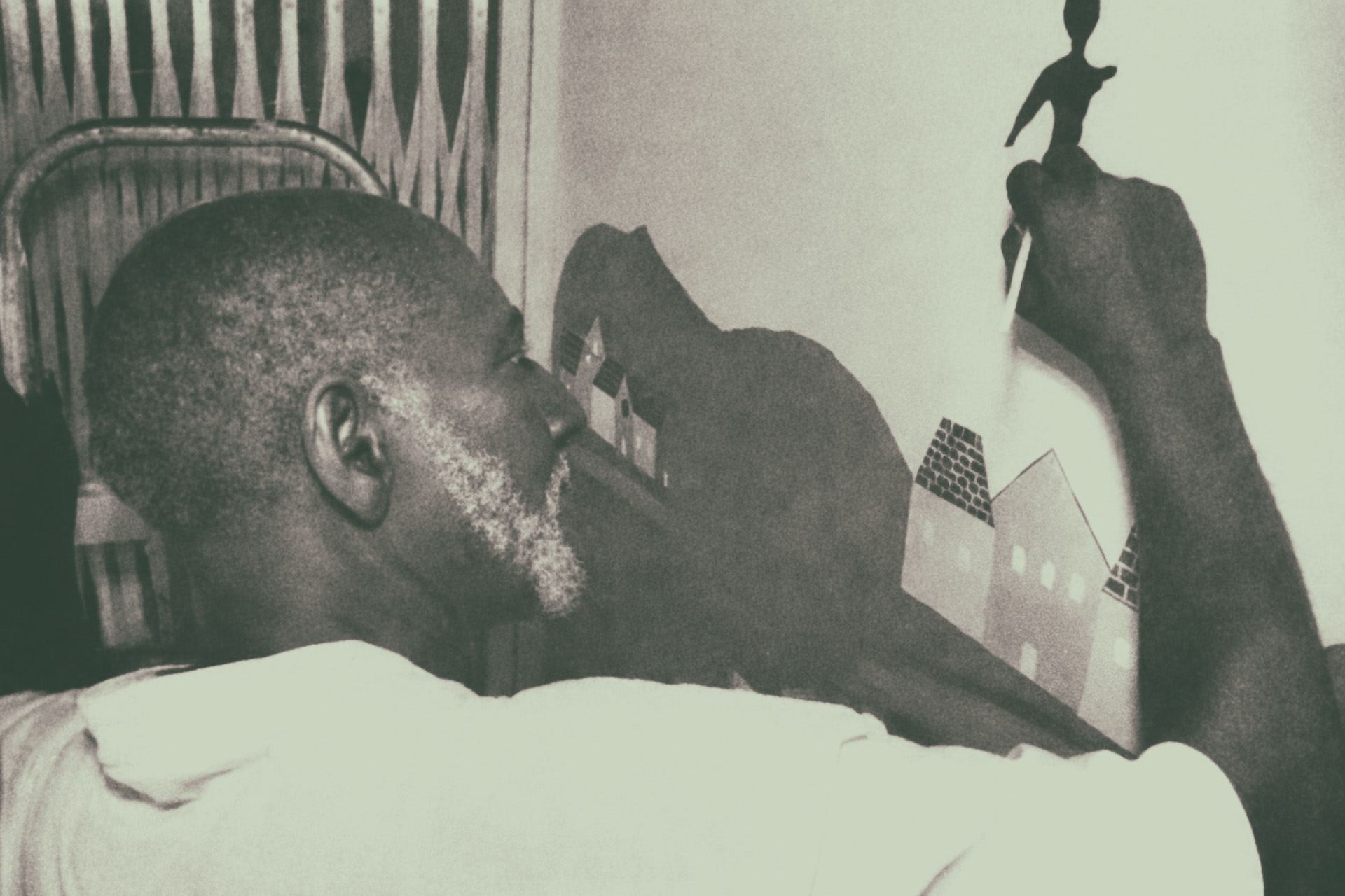 Nélson Sargento de perfil pintando um painel com casas e figura humana na parede da residência de Roberto Esquenasi