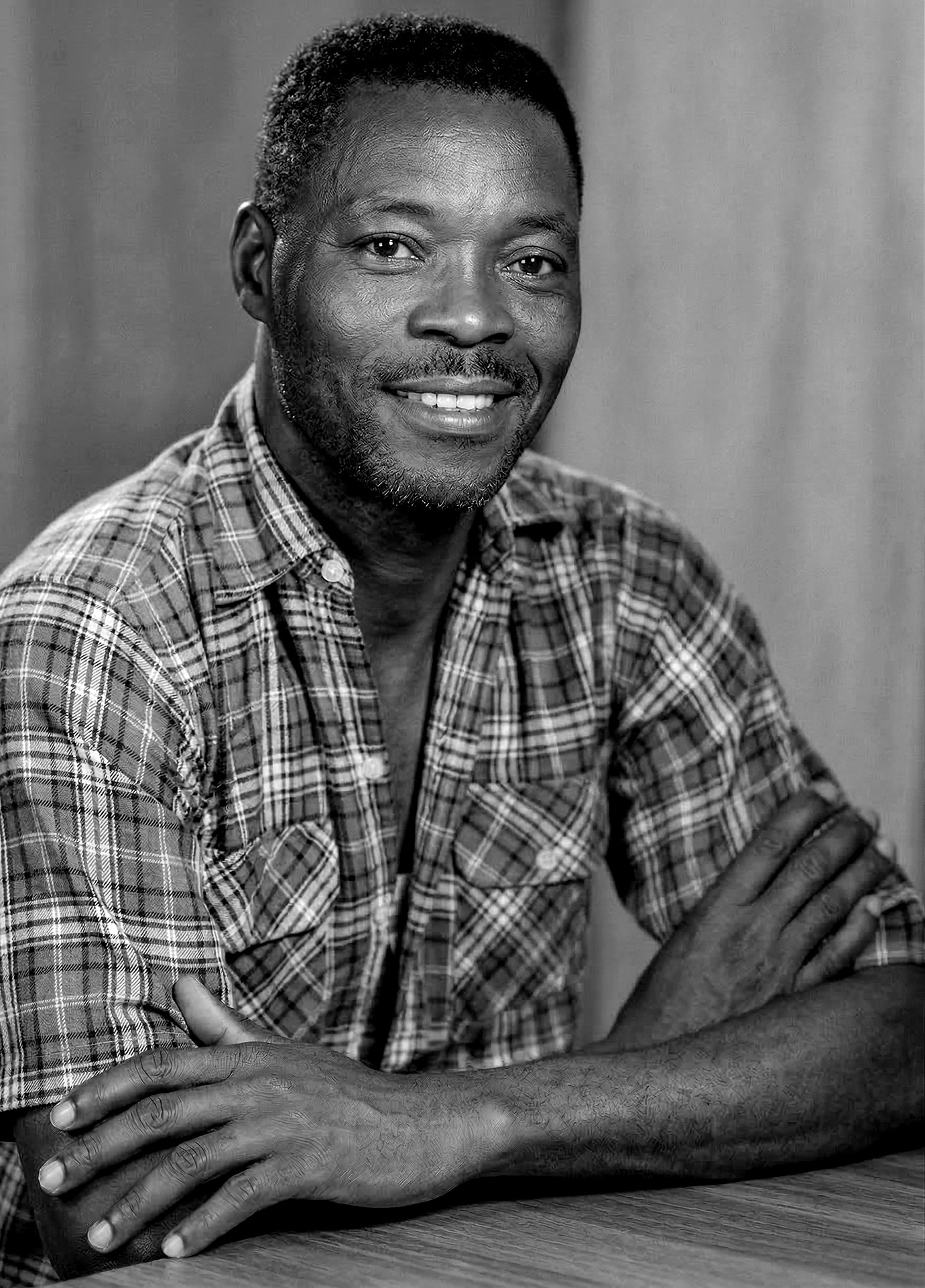 Retrato de Geraldo Pereira da Mangueira sorrindo com camisa xadrez e braços apoiados sobre a mesa