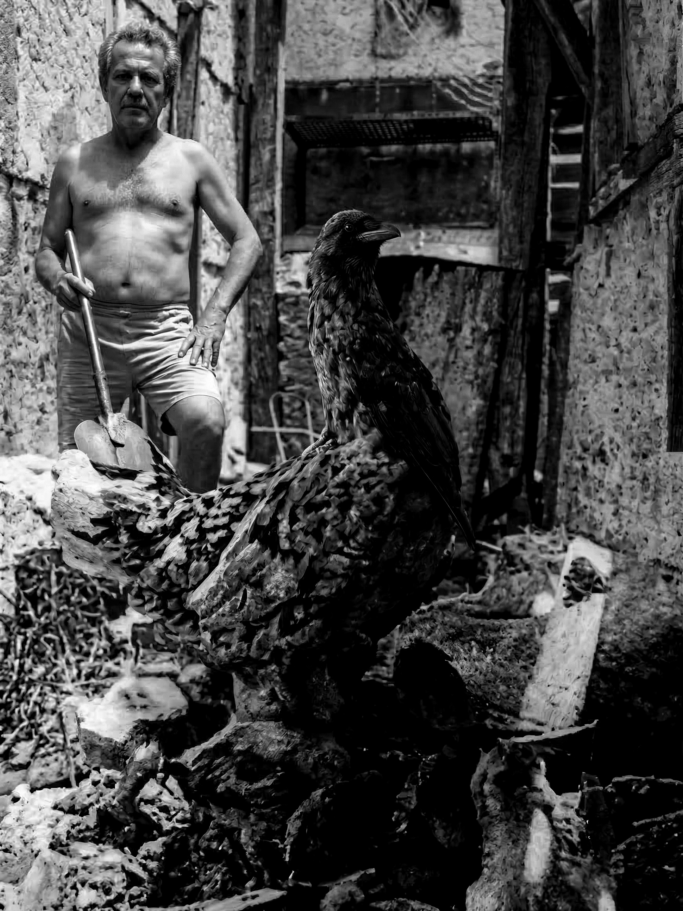 Melão sem camisa segurando uma enxada no barracão da Mangueira, com uma galinha preta de grande porte em primeiro plano
